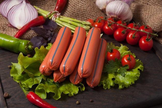 Salsicce bollite su una tavola di legno decorata con verdure fresche