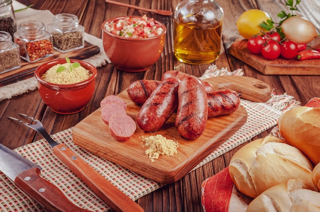 Salsicce brasiliane alla griglia sulla tavola di legno con pane, insalata, farofa e ingredienti