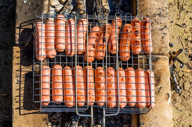 Salsicce che cucinano in una griglia del barbecue sul fuoco di accampamento