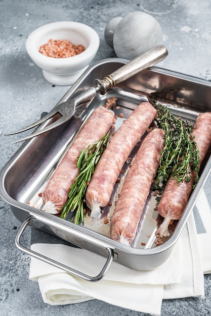 Salsicce crude di carne di maiale Bratwurst in un vassoio da cucina. Sfondo grigio. Vista dall'alto.