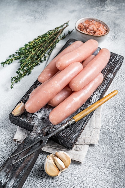 Salsicce crude di carne di tacchino e di pollo su una tavola di legno con timo. Sfondo bianco. Vista dall'alto.