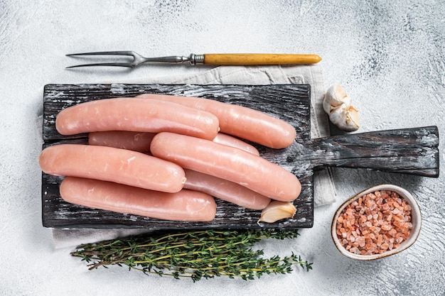 Salsicce crude di carne di tacchino e di pollo su una tavola di legno con timo. Sfondo bianco. Vista dall'alto.