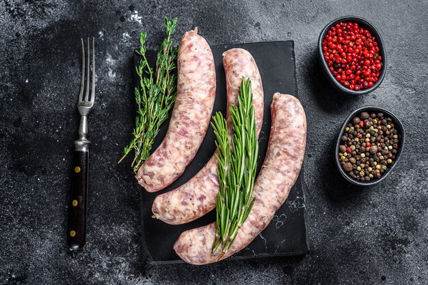 Salsicce di carne di maiale fatte in casa crude in pelli con erbe aromatiche. Vista dall'alto. Sfondo nero.