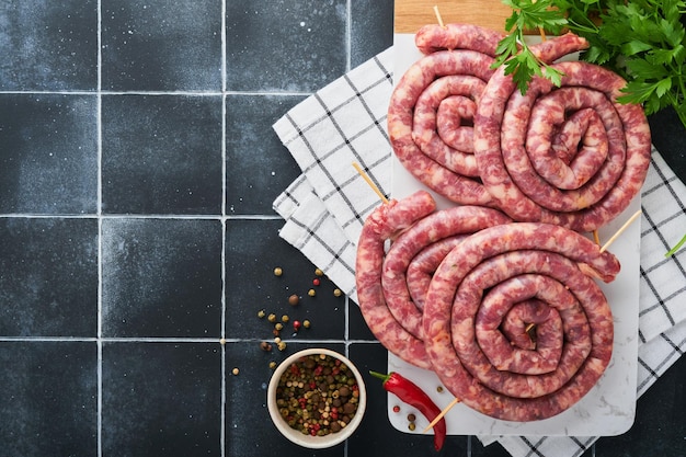 Salsicce di maiale a spirale crude Salsicce di maiale fresche gustose spirali attorcigliate per barbecue su supporto bianco con spezie ed erbe aromatiche per la cena di festa dell'Oktoberfest su sfondo grigio Vista dall'alto Set dell'Oktoberfest