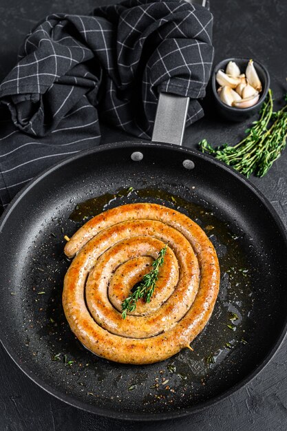 Salsicce fritte a spirale con aglio e condimento in padella. Vista dall'alto.