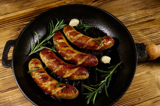 Salsicce fritte con aglio rosmarino e spezie in padella in ghisa su tavola di legno Vista dall'alto