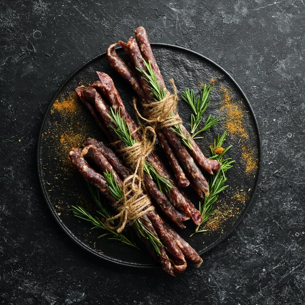 Salsicce salate essiccate con rosmarino e spezie Kabanosy Su uno sfondo di pietra nera Vista dall'alto