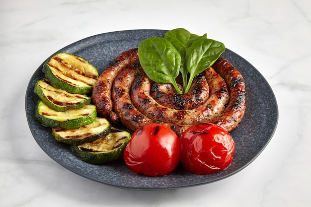 Salsiccia a spirale alla griglia con zucchine e pomodori ed erbe aromatiche su un piatto scuro fatto a mano