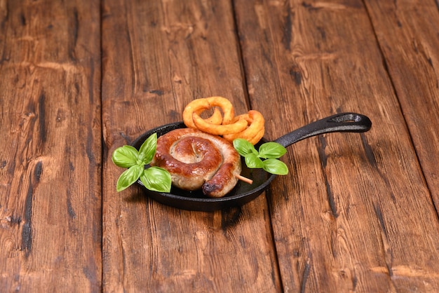 Salsiccia a spirale piccante arrosto con foglie di basilico e patatine fritte in padella