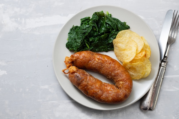 Salsiccia affumicata fritta con patatine fritte e verdure sul piatto bianco su fondo in ceramica