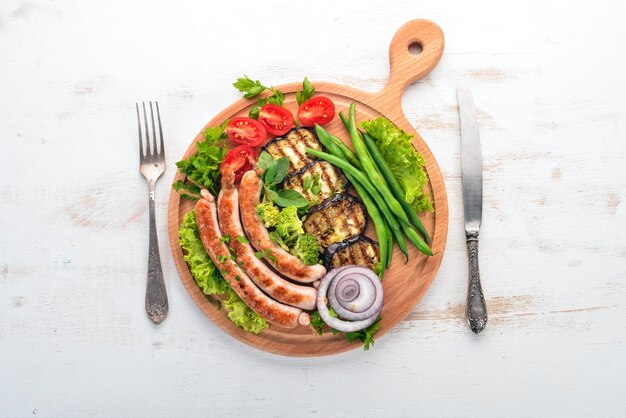 Salsiccia alla griglia con melanzane e pomodori a bordo Cibo sano su un tavolo di legno bianco Vista dall'alto Spazio libero per il testo