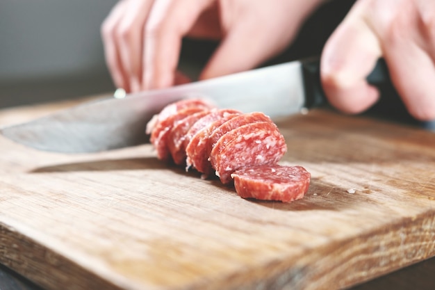 Salsiccia, coltello, mani di donna, affettare salsiccia, pezzi spessi, tavola di legno, coltello in mani femminili, donna taglia la salsiccia