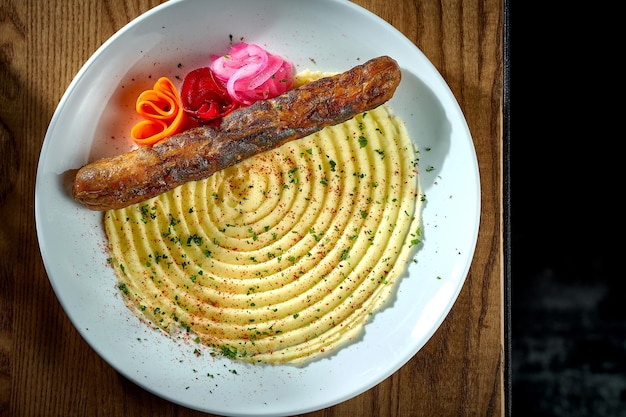 Salsiccia di carne bavarese con un contorno di cipolle di purè di patate in un piatto su un bratwurst di fondo di legno