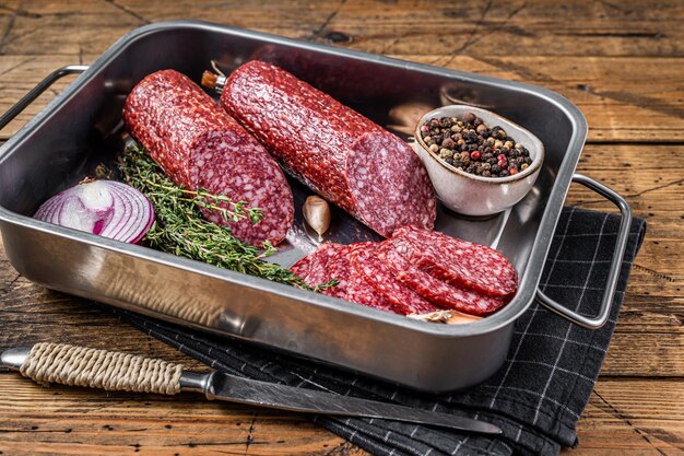 Salsiccia di salame secco affettato italiano in vassoio d'acciaio. Fondo in legno. Vista dall'alto.