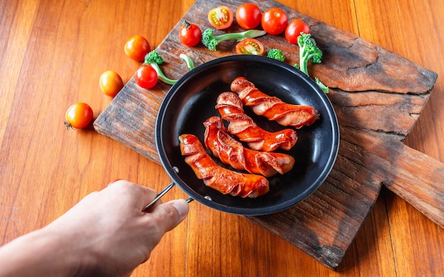 Salsiccia fritta in una padella nera nelle mani dello chef