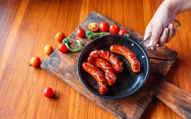 Salsiccia fritta in una padella nera nelle mani dello chef