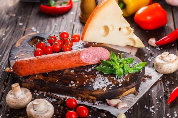 salsiccia secca fatta in casa, basilico e aglio, intero e pezzo, spezie e verdure sul tagliere