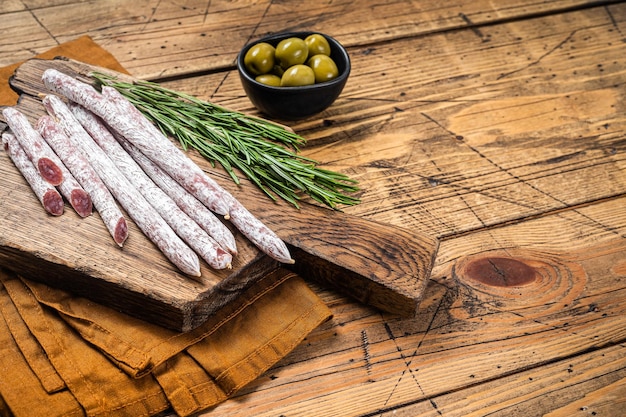 Salsiccia spagnola di salame secco Fuet con rosmarino su tagliere di legno Sfondo in legno Vista dall'alto Spazio di copia