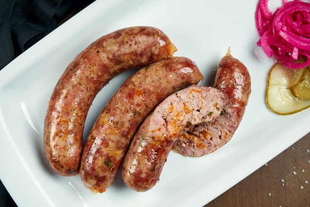 Salsiccia tritata succosa appetitosa di maiale alla griglia in un fumatore con formaggio cheddar in un piatto bianco con verdure in scatola. Merenda con birra tedesca