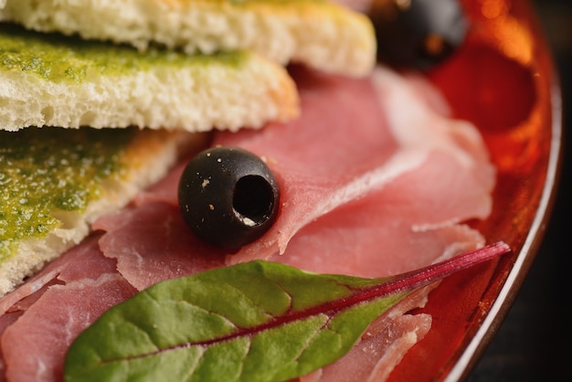 Salsiccie, jamon e prosciutto assortiti con le fette di pane fritto su un piatto rosso. Su un tavolo di legno