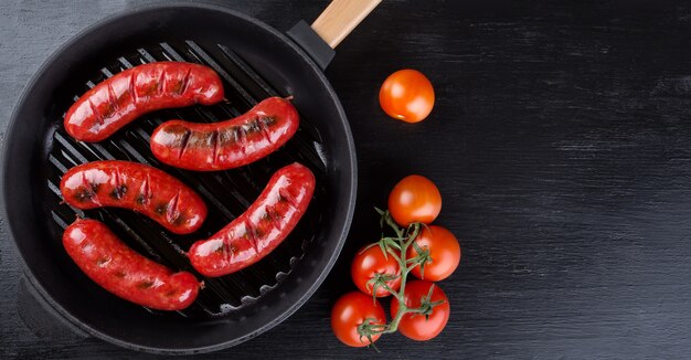 Salsiccie succose fritte su una padella nera con i pomodori