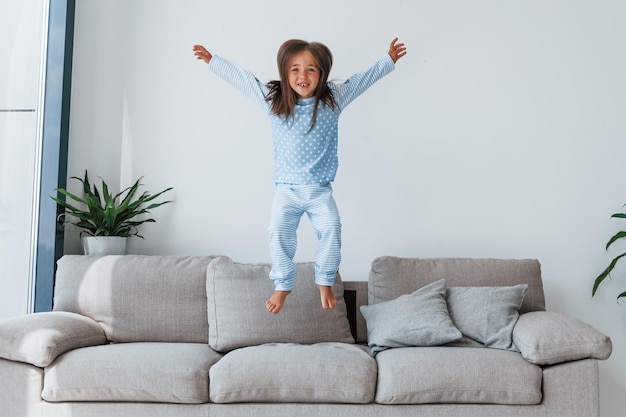 Saltando sul divano Bambina carina al chiuso a casa da sola Bambino che si gode il fine settimana