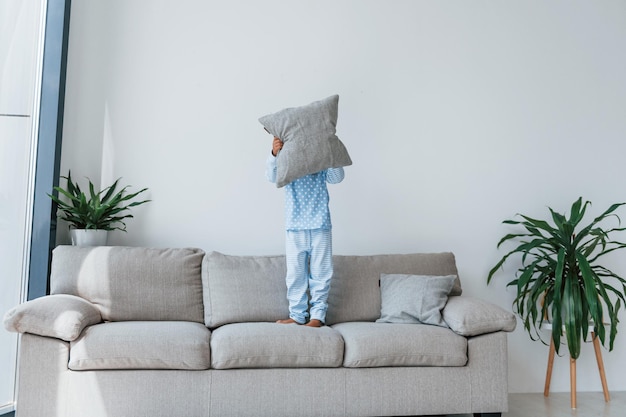 Saltando sul divano Bambina carina al chiuso a casa da sola Bambino che si gode il fine settimana