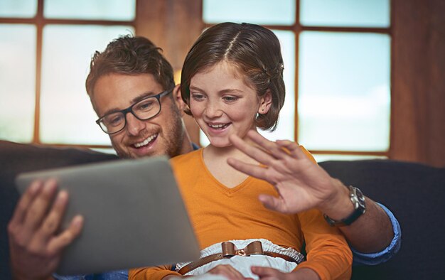 Salutare la famiglia in tutto il mondo Foto di un padre e una figlia che usano insieme una tavoletta digitale sul divano di casa