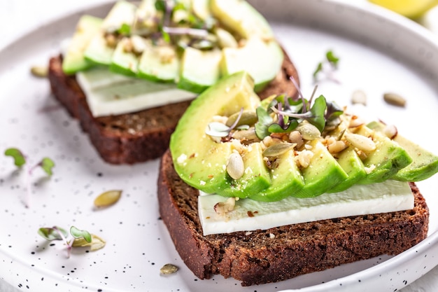 Salutari toast di avocado con pane di segale, avocado a fette, formaggio, zucca, noci e sesamo per colazione o pranzo