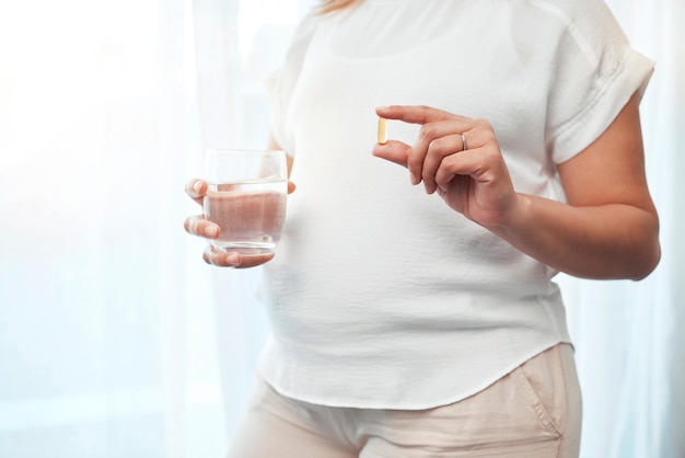 Salute della gravidanza e donna con pillole e acqua per il benessere vitamine e cure mediche per il bambino Medicina sanitaria e mani della donna incinta con vetro che assumono minerali e integratori di farmaci