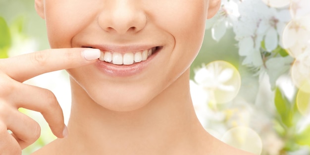 salute dentale, bellezza, igiene e concetto di persone - primo piano del volto di donna sorridente che punta ai denti su sfondo naturale verde