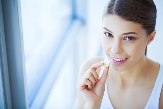 Salute e bellezza Vitamine Bella ragazza con i denti bianchi che tiene una pillola nelle mani