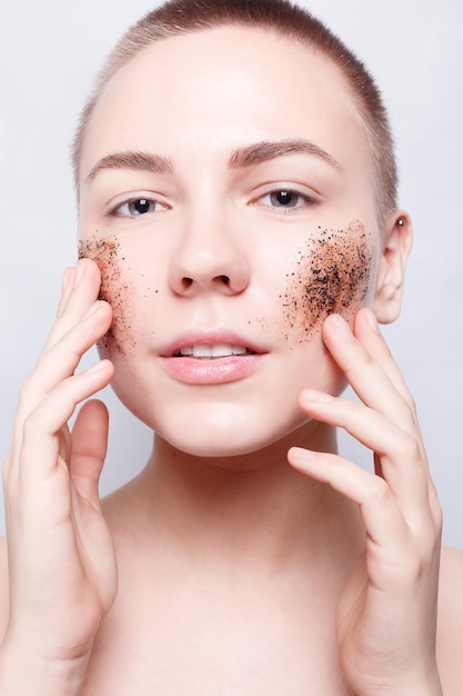 Salute, persone, cura della pelle, giovinezza e concetto di bellezza - Donna sorridente con i capelli corti, calva pulisce la pelle caffè skrub, foto in studio, ritratto ravvicinato. Pelle fresca pulita da vicino. Spa donna sorridente