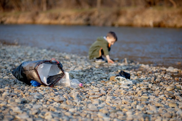 Salva il concetto di ambiente un ragazzino che raccoglie immondizia e bottiglie di plastica sulla spiaggia per scaricarle nella spazzatura