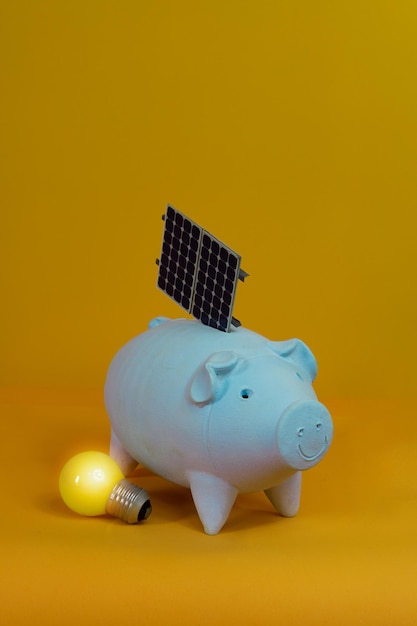 Salvadanaio e pannello solare fotovoltaico isolato su sfondo giallo. Immagine finanza fotovoltaica.