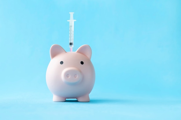 Salvadanaio e siringa medica con soldi su sfondo blu. Il concetto di risparmio sulla salute. Vaccinazione costosa. la crisi economica in sanità. economia malata.