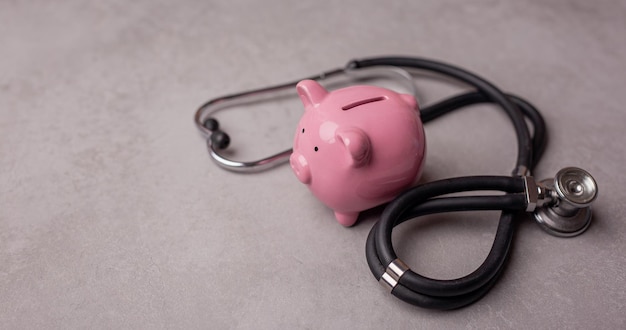 Salvadanaio rosa e stetoscopio su sfondo grigio Concetto di come risparmiare sull'assicurazione sanitaria