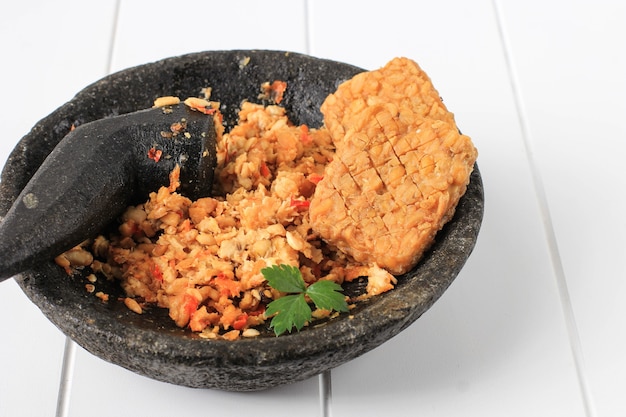 Sambal Tempeh, Tempe schiacciato piccante su pestello di pietra. Cibo tradizionale indonesiano con gusto piccante e salato. Copia spazio su sfondo di legno bianco