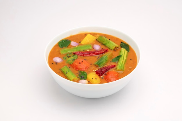 Sambar, curry vegetariano misto disposto in una ciotola bianca su fondo bianco strutturato.