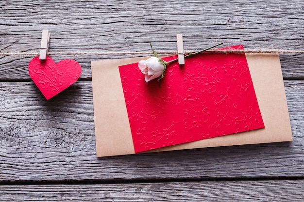 San Valentino con cuore di carta rossa e biglietto di auguri vuoto su mollette su assi di legno rustico