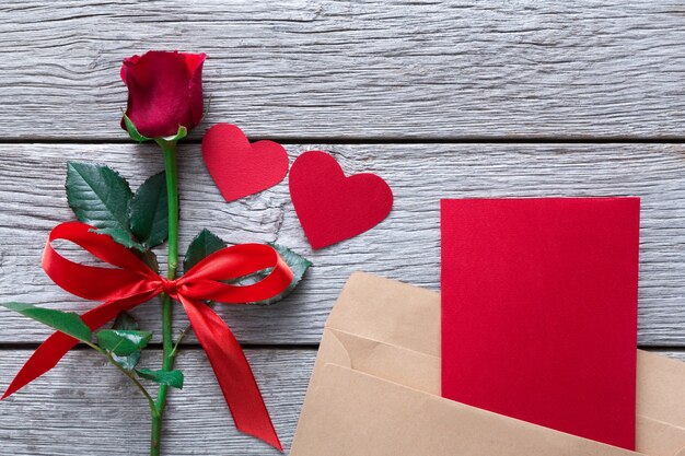 San Valentino con fiore rosa rosso e cuori di carta fatta a mano e biglietto di auguri in busta su legno rustico