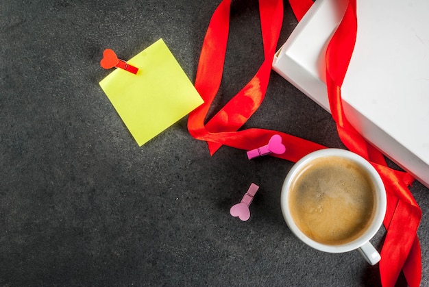 San Valentino, confezione regalo con nastro rosso, tazza da caffè, nota di carta bianca per congratulazioni con spille a forma di cuore, vista nera e superiore