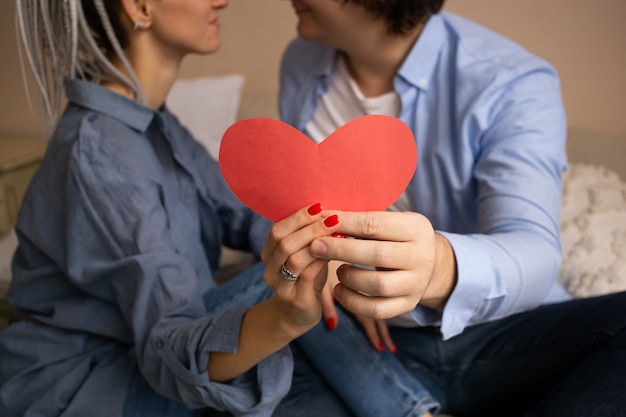 San Valentino cuore rosso nelle mani. Coppia in camera da letto seduto sul letto e abbracciare.