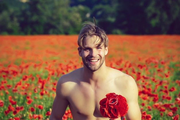 San Valentino. Felice uomo nudo con bouquet. Ragazzo sorridente muscoloso nel campo del papavero rosso, primavera