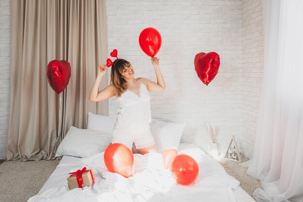 San Valentino, festa della donna. Giovane ragazza caucasica seduta a letto e festeggia San Valentino con in mano un palloncino a forma di cuore