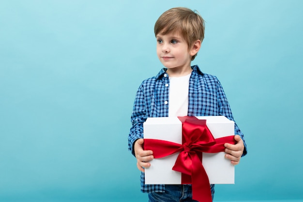 San Valentino . il bambino attraente tiene un grande regalo con un nastro rosso su un azzurro