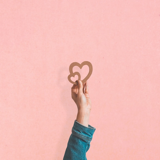 San Valentino, mano femminile che tiene il simbolo del cuore in legno sul muro rosa pallido. Concetto di amore. design minimale.