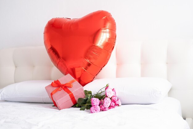 San Valentino sfondo grande cuore rosso palloncino confezione regalo e bouquet di rose rosa su biancheria da letto bianca
