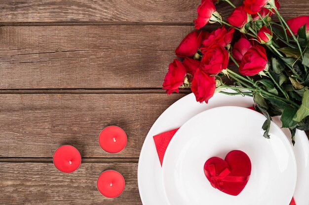 San Valentino tavola da pranzo con nastro rosso, rose, coltello e forchetta e anello su sfondo di quercia. Natura morta