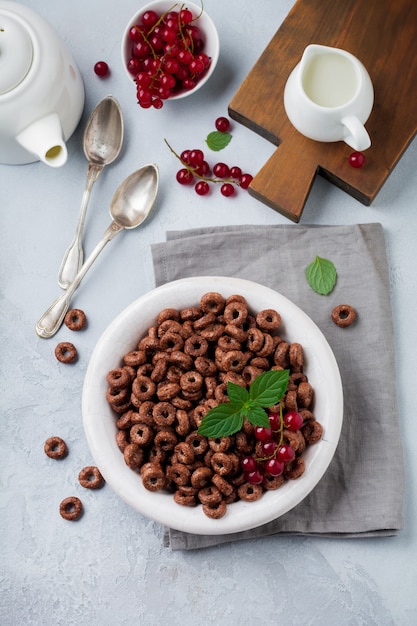 Sana colazione con anelli di mais al cioccolato, bacche di ribes rosso, yogurt e tè su uno sfondo grigio cemento